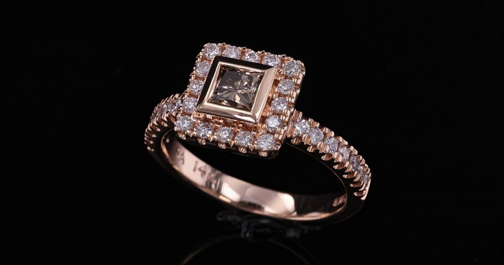 Rose gold ring featuring a square princess-cut cognac diamond center stone, framed by a halo of white diamonds and a diamond-studded band, displayed on a black background.