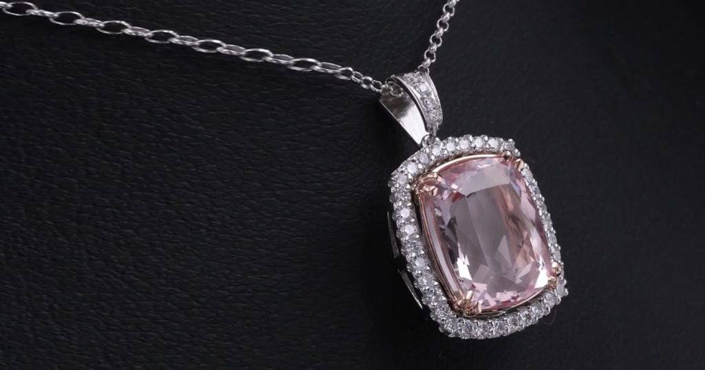 Close-up of a cushion-cut morganite pendant set in white gold with a diamond halo, hanging on a silver chain against a black background.