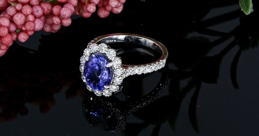 Elegant white gold ring with an oval-cut tanzanite center stone, surrounded by a halo of diamonds and a diamond-studded band.