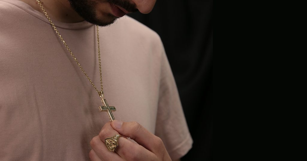 Man holding a gold cross necklace close to his chest while wearing a Christian ring