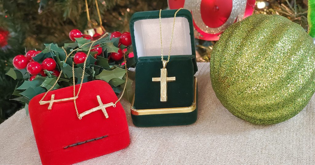 Gold cross necklaces displayed in festive gift boxes with Christmas decorations.