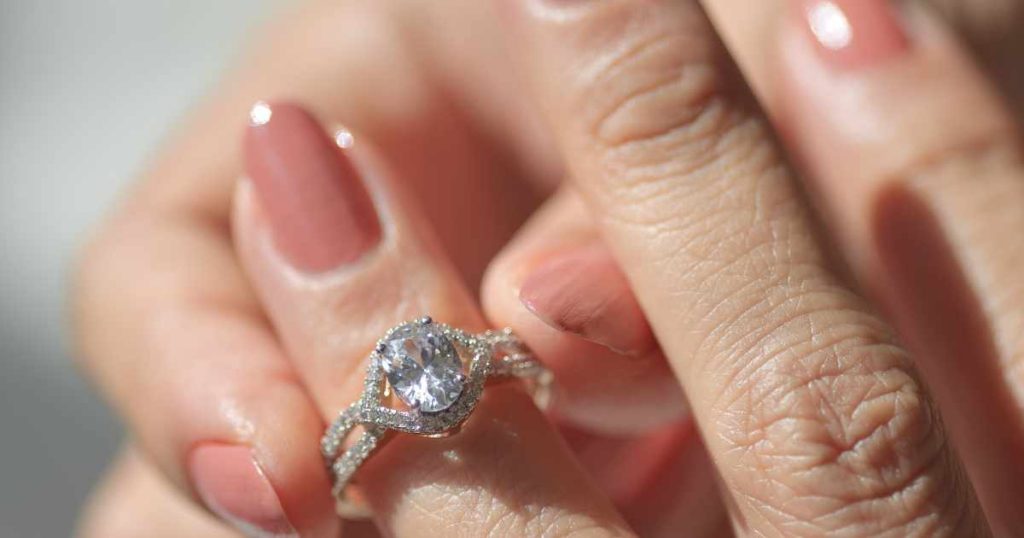 Close-up of a hand wearing a diamond engagement ring with a sparkling halo and twisted band design.