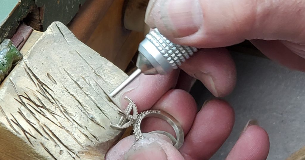 Jeweler handcrafting a diamond ring setting with precision tools at a workbench.