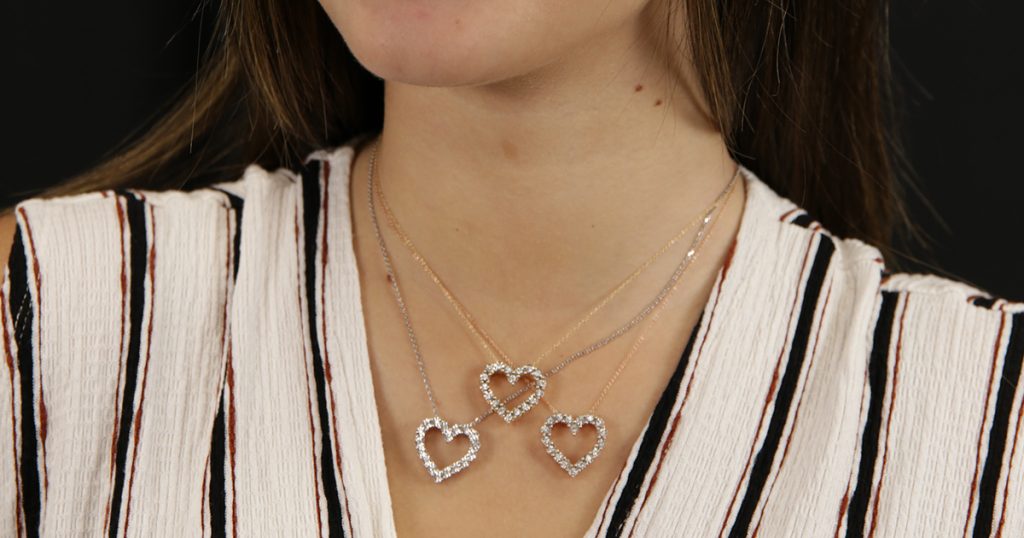 Close-up of a woman wearing three diamond heart necklaces layered together on delicate gold and silver chains, styled with a striped blouse.
