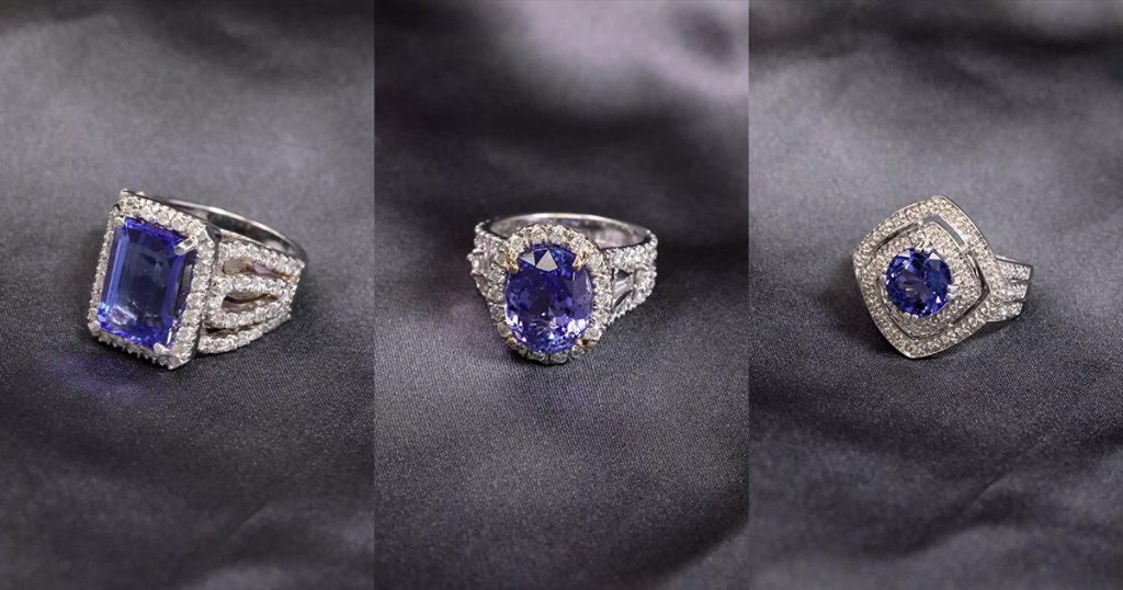 Three breathtaking Tanzanite rings displayed on a smooth satin background. Featuring emerald, oval, and cushion cuts surrounded by shimmering diamonds, symbolizing grace and luxury.