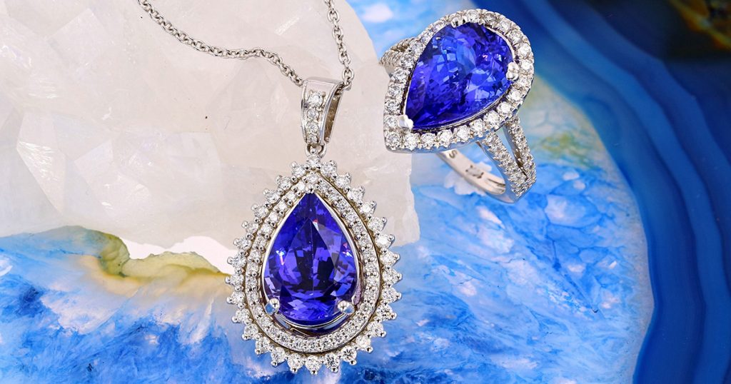 Pear-shaped Tanzanite pendant and matching ring set in white gold with diamond halos on crystal background.