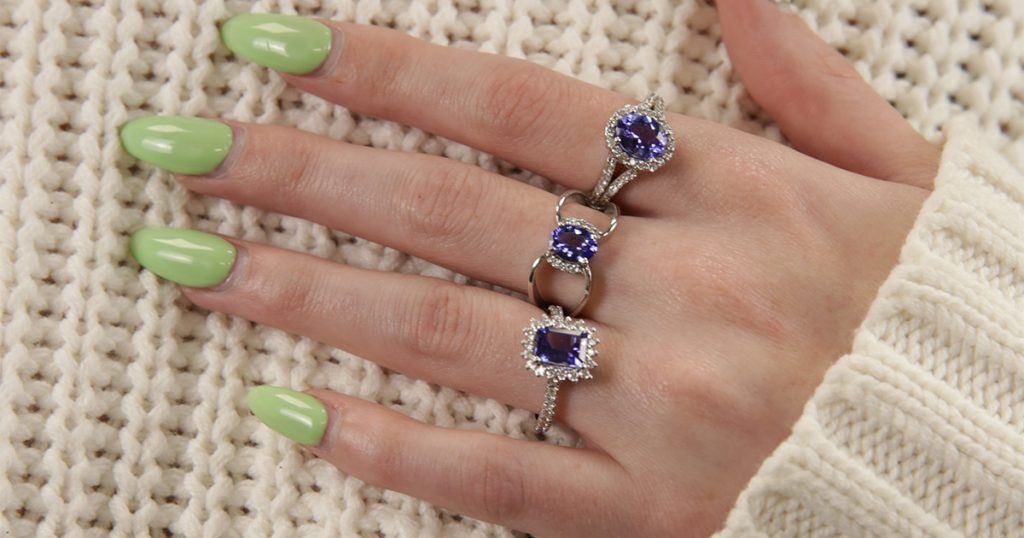 Hand wearing multiple Tanzanite rings with diamond halos on a knit background.