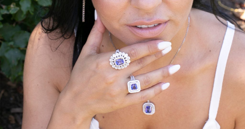 A close-up of a woman wearing luxurious Sophia Fiori Tanzanite rings, each surrounded by sparkling diamond halos. The vivid violet-blue hue of Tanzanite radiates elegance and sophistication, perfect for collectors of rare gemstones.