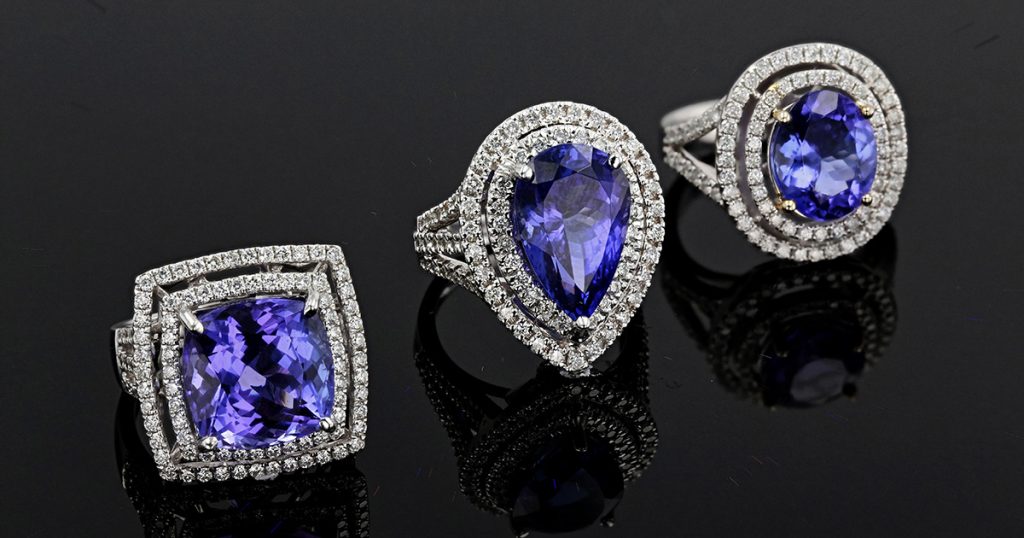 Trio of Tanzanite statement rings in white gold with diamond accents on black reflective background.