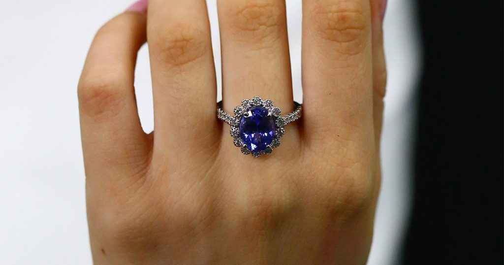 Oval Tanzanite engagement ring with diamond halo worn on a hand.